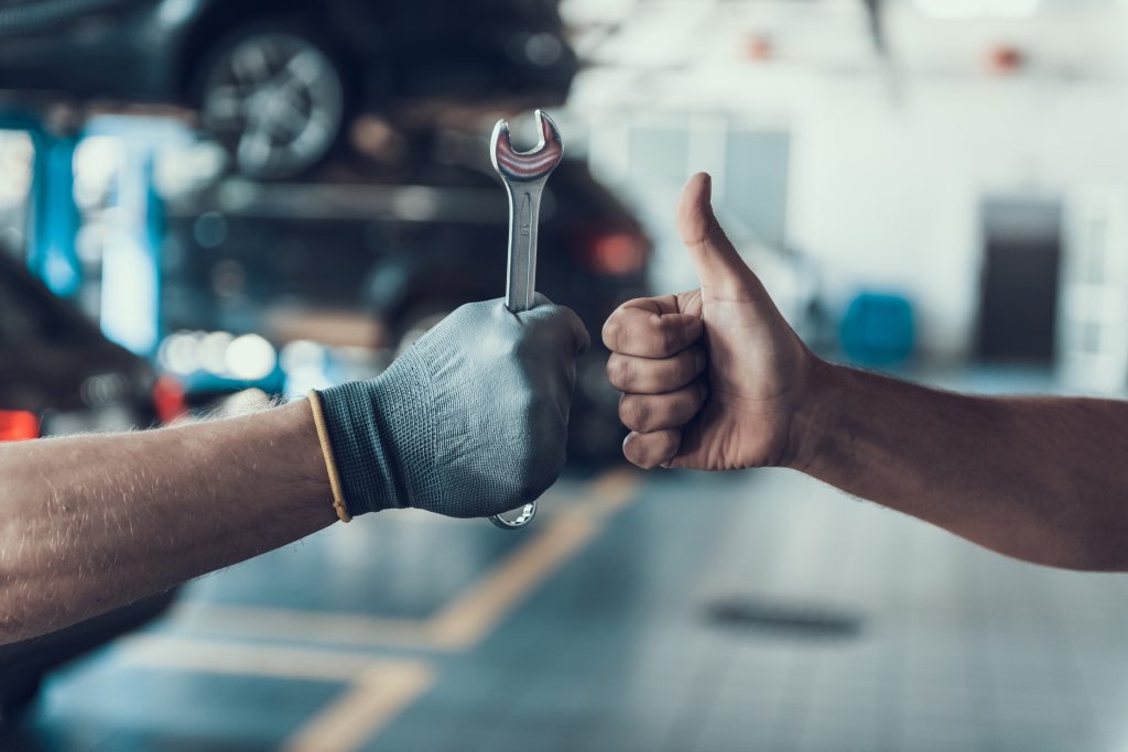 A mechanic handing over a wrench while another person gives a thumbs-up.